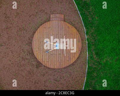 Drone shot di donna che si trova sul palco di legno nel parco Foto Stock