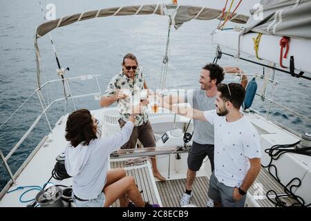 Gli amici tostano la birra mentre si gustano a bordo di una barca a vela in mare