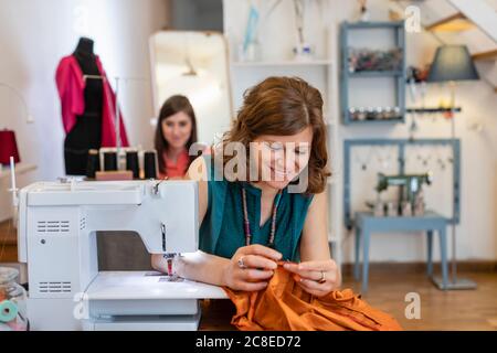 Sorridente femmina su misura guardando il tessuto da macchina da cucire in studio di design Foto Stock