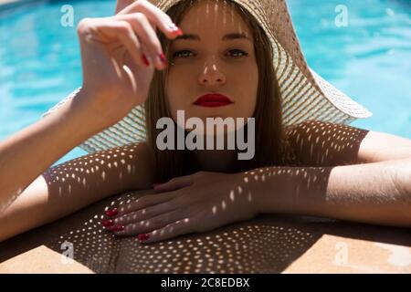 Primo piano di una giovane donna che indossa un cappello che si rilassa a bordo piscina durante giorno di sole Foto Stock