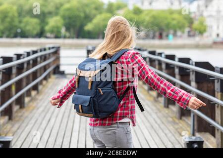 Donna felice che indossa una camicia controllata con lo zaino che gira sul ponte Foto Stock