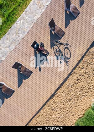 Russia, Tikhvin, uomo in bicicletta sul lungomare con lettini, vista aerea Foto Stock