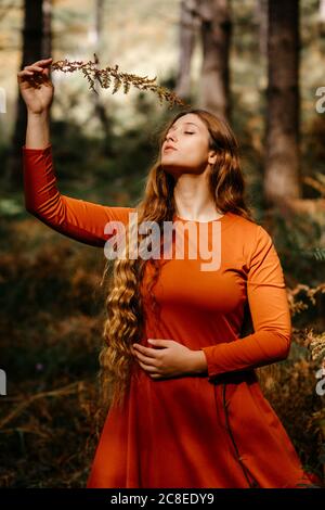 Bella donna con gli occhi chiusi tenendo le foglie mentre si sta in piedi bosco Foto Stock