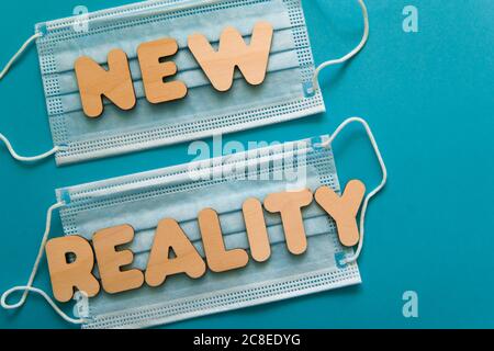 NUOVE parole DI REALTÀ sulle maschere facciali protettive su sfondo blu. Dopo covid-19 pandemie cambiamenti, nuova normale, indossare maschera viso in concetto pubblico. Foto Stock