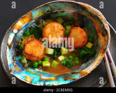 Capesante scottate servite in conchiglia di abalone con verdure, mele verdi e una salsa al burro marrone al limone Foto Stock