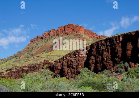 Paesaggio Outback in lontanissima campagna Australia, con la catena montuosa di roccia rossa, verde cespuglio e cielo estivo azzurro come sfondo. Foto Stock