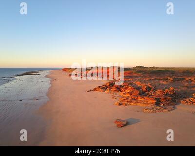 Vista panoramica aerea della costa remota vicino a Broome, Australia Occidentale, con oceano, spiaggia, scogliere rosse, paesaggio dell'entroterra e cielo blu tramonto come c Foto Stock