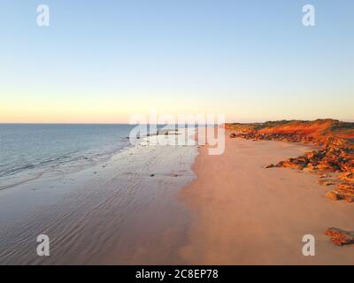 Vista panoramica aerea della costa remota vicino a Broome, Australia Occidentale, con oceano, spiaggia, scogliere rosse, paesaggio dell'entroterra e cielo blu tramonto come c Foto Stock