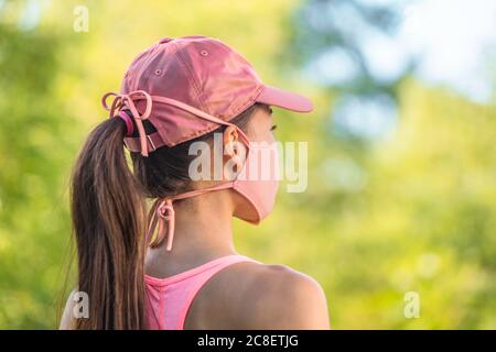 Corona virus maschera viso COVID-19 giovane donna sana all'aperto a piedi indossando cravatte in tessuto con cappuccio sportivo rosa. Stile di vita estivo Foto Stock