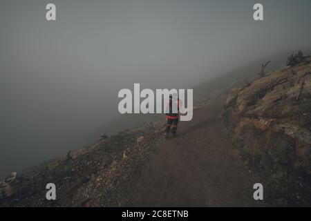 Una guida di Kawah Ijen che cammina da sola sul cratere di Kawah Ijen sulla strada che l'abbondanza di smog a Giava, Indonesia. Foto Stock