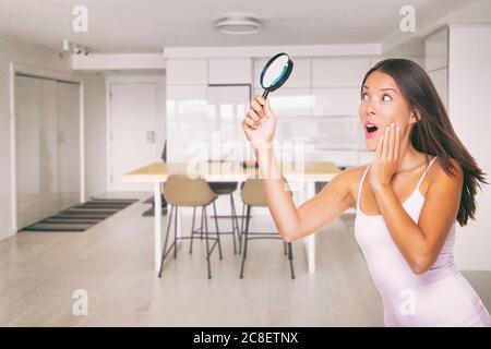 Nuova casa acquirente immobiliare Asian donna felice impressionato con moderno arredamento condominio urbano. Ragazza che guarda la casa con lente d'ingrandimento divertente Foto Stock