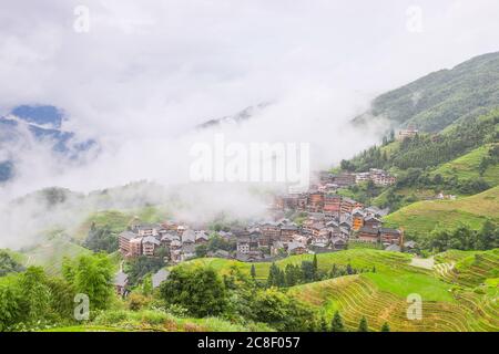 Pittoresche risaie a terrazze e case di villaggio a Jinkeng, Longji, Guangxi, Cina durante una giornata torbida e nuvolosa con occasionali precipitazioni Foto Stock