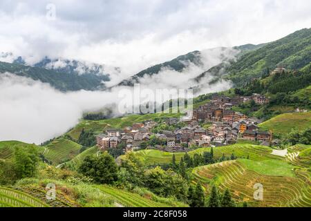 Pittoresche risaie a terrazze e case di villaggio a Jinkeng, Longji, Guangxi, Cina durante una giornata torbida e nuvolosa con occasionali precipitazioni Foto Stock