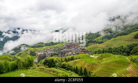 Pittoresche risaie a terrazze e case di villaggio a Jinkeng, Longji, Guangxi, Cina durante una giornata torbida e nuvolosa con occasionali precipitazioni Foto Stock