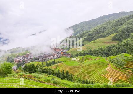 Pittoresche risaie a terrazze e case di villaggio a Jinkeng, Longji, Guangxi, Cina durante una giornata torbida e nuvolosa con occasionali precipitazioni Foto Stock