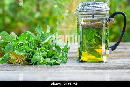Composizione di tè alla menta fresco in una teiera di vetro su un tavolo di legno. Foto Stock