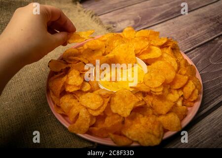 La ragazza prende un chip da un piatto rotondo con patatine e una pentola con salsa di formaggio al centro del piatto. Primo piano Foto Stock