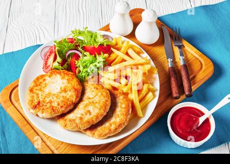 insalata di pomodoro e patatine fritte servite con tre hamburger di tacchino freschi fritti su un piatto bianco su un tagliere con salsa di pomodoro in ciotola, ho Foto Stock