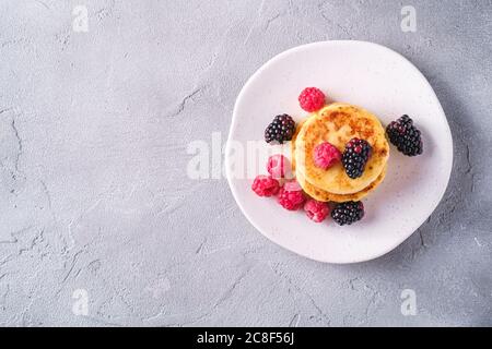 Frittelle al formaggio, frittelle di cagliata dessert con lampone e frutti di mora in piastra su fondo di pietra in cemento, spazio copia vista dall'alto Foto Stock