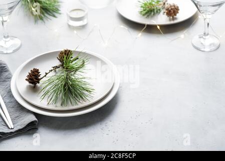 Tavolo Natale con rami di pino e coni su tavolo grigio chiaro, spazio copia. Cena di Natale, design per feste, concetto. Foto Stock