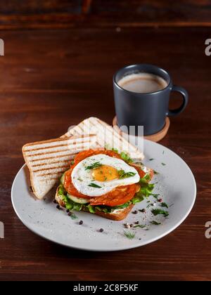 Sandwich club con prosciutto, pancetta, ripieno di pomodoro, cetrioli sottaceto, uova arrosto, formaggio, salsa e insalata. Il sandwich viene tagliato a metà in due triangoli. Primo piano. Sfondo scuro. Foto Stock