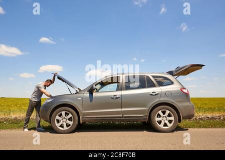 Un'auto con cofano aperto e un giovane confuso sulla strada. Foto Stock
