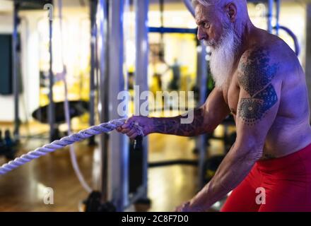 Allenamento uomo anziano con corda da battaglia all'interno della palestra - allenamento maschile maturo nel centro benessere Foto Stock