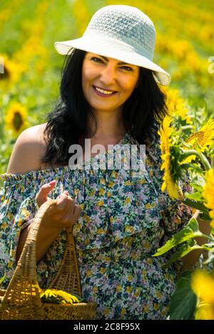 Donna felice con cappello in campo girasoli che tiene il cesto Foto Stock