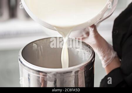 Close-up della mano di un lavoratore che riempie il latte fresco da un serbatoio del latte - Preparazione del latte per gelato in un moderno caseificio fabbrica - Fotografia macro Foto Stock