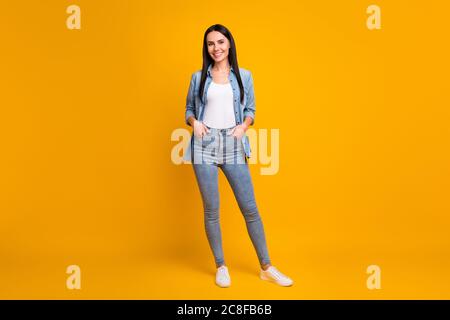 Vista completa del corpo di bella bella bella bella bella bella e allegra ragazza cheery che indossa abiti casual che si pone tenendo le mani in tasche isolato su luminoso Foto Stock