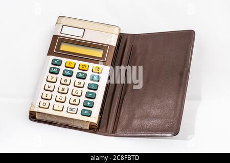 Vecchia calcolatrice tascabile elettronica in una custodia di plastica marrone su sfondo bianco. Foto Stock