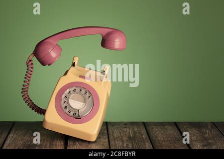 Telefono retro rotante giallo e rosa girato su un tavolo di legno su sfondo verde. Fotografato quando una chiamata viene attraverso e il ricevitore f Foto Stock