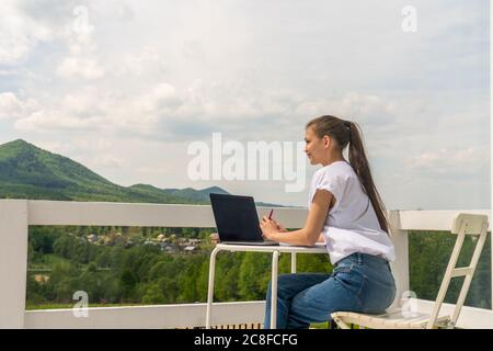 Una donna di affari positiva di successo della brunetta è seduta su una terrazza esterna con un taccuino in un lettino solare Foto Stock