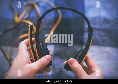 Un uomo sta tenendo grandi cuffie gialle con un lungo filo aggrovigliato e sta per ascoltare la musica. Pausa musica. Foto Stock