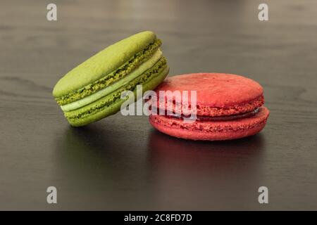 Lamponi dolci e macaroni al pistacchio isolati su sfondo di legno scuro. Pasticceria francese. Piccoli deliziosi dolci francesi. Dessert francese tradizionale Foto Stock