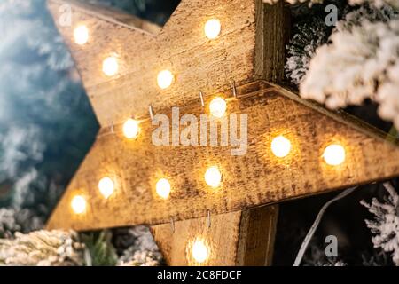 Stella decorativa in legno con lampade appese su rami di pino con sfondo festoso. Foto Stock