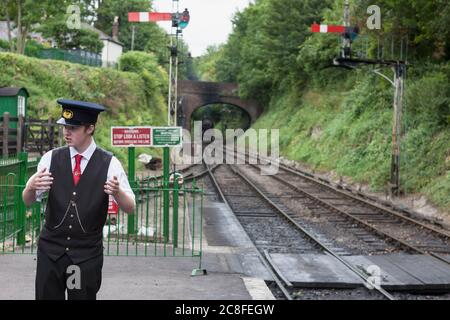 Treno in avvicinamento alla stazione di Alresford sulla Ferrovia a vapore Mid-Hants (linea di Watercress), Hampshire, Inghilterra, Regno Unito: Il giovane maestro della stazione in presenza Foto Stock