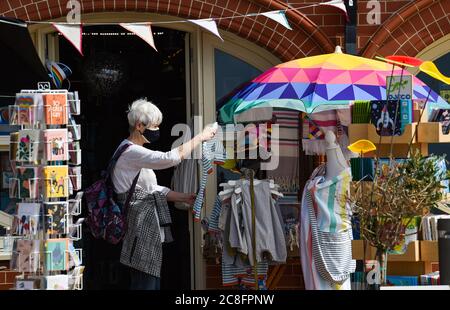 Brighton UK 24 luglio 2020 - questo acquirente indossa una maschera facciale mentre naviga all'esterno di un negozio di fronte al mare a Brighton oggi dopo che nuove normative sono state introdotte dal governo a mezzanotte in Inghilterra nella lotta contro il coronavirus COVID-19 pandemia : Credit Simon Dack / Alamy Live News Foto Stock