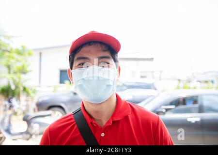 I militari asiatici che indossano una divisa rossa con un cappuccio rosso e maschera facciale che manipolano scatole di cartone da dare alla cliente femminile di fronte alle ore Foto Stock