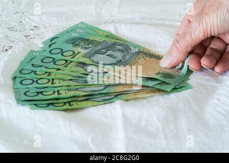 Persona che mette e contando i soldi, cento banconote del dollaro, valuta australiana Foto Stock