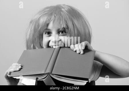 Ragazza morde grande libro blu. Ragazza della scuola con faccia felice isolata su sfondo rosa. Torna a scuola e concetto di istruzione. Alunno in uniforme scolastica con parrucca rosa. Foto Stock