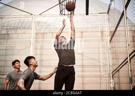 giovani uomini adulti asiatici che giocano a basket sul campo all'aperto Foto Stock