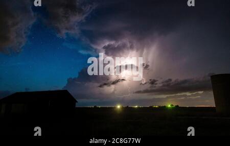Numerosi fulmini da nuvola a nuvola si vedono lungo la linea secca di notte, con stelle sullo sfondo sopra gli edifici della fattoria Foto Stock