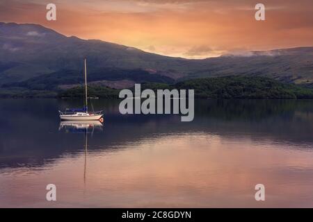 Barca a vela riposante a Loch Lomond, Scozia, in una serata al tramonto Foto Stock