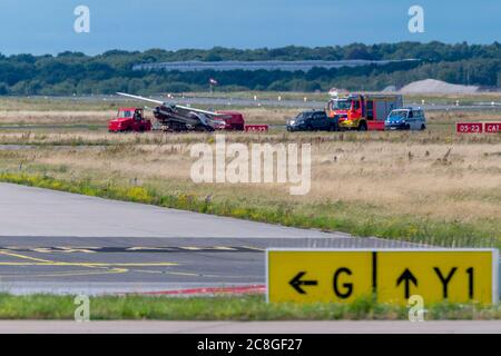 Amburgo, Germania. 24 luglio 2020. Il piccolo aereo in crash viene trasportato via su un rimorchio mentre i veicoli di emergenza guidano sopra il campo aereo. Venerdì un piccolo aereo si è schiantato dalla pista dell'aeroporto Helmut Schmidt, causando la chiusura completa delle piste. Credit: Jonas Walzberg/dpa/Alamy Live News Foto Stock