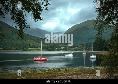 Sotto un pesante cielo grigio, yacht ormeggiati in una tranquilla insenatura sulle rive del lago di Loch Leven. Foto Stock