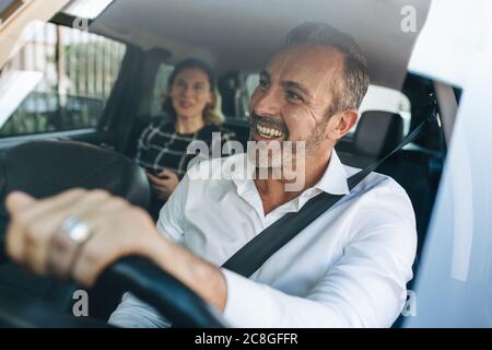 Tassista che parla con una donna che siede sul sedile posteriore. Donna d'affari che usa il taxi per andare al lavoro. Foto Stock