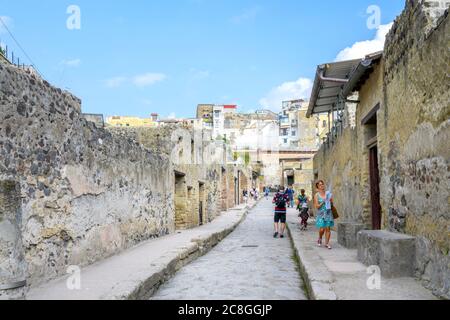Si cammina lungo una strada tra edifici nella città romana di Ercolano, parzialmente distrutta dall'eruzione del Vesuvio nel 79 d.C. Foto Stock