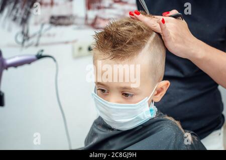 Nuovo normale adattamento alla vita normale dopo blocco pandemico. Ragazzo ottenere capelli tagliati indossare maschera. Foto Stock