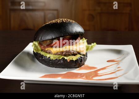 Cheeseburger nero con paty di manzo su piatti quadrati e tavolo di legno Foto Stock